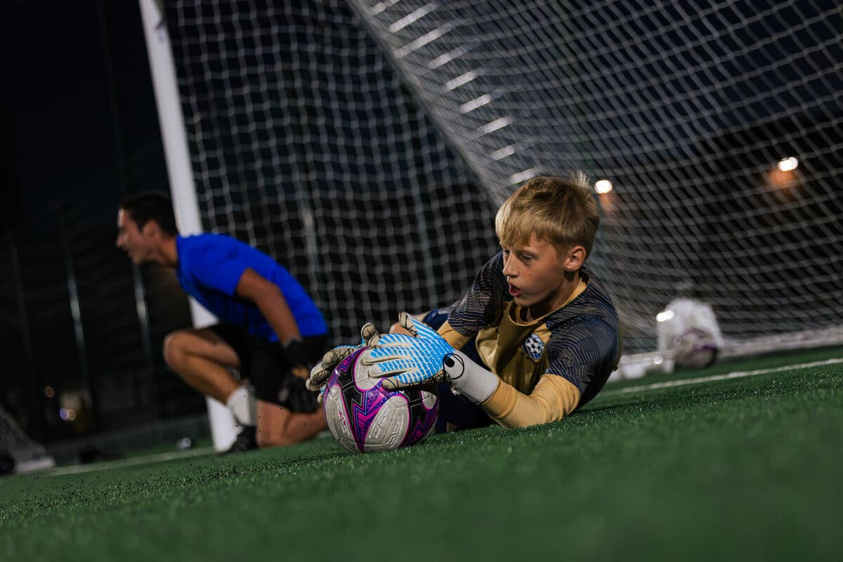 A goalkeeper gathering the ball at a coach's feet
