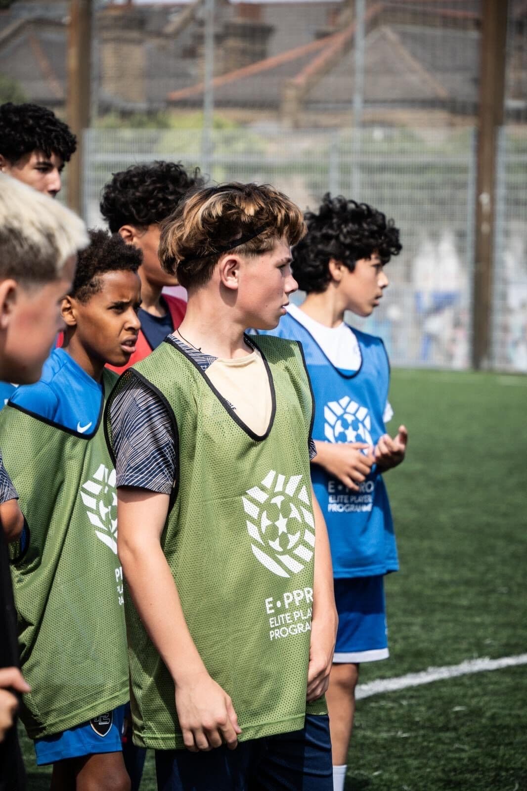 A line of players in E-PPRO bibs listening to a coach